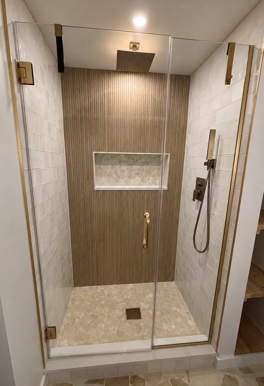 Walk-in shower in a Barrington bathroom remodel featuring vertical wood-look tile, brass fixtures, glass enclosure, and mosaic shower floor.