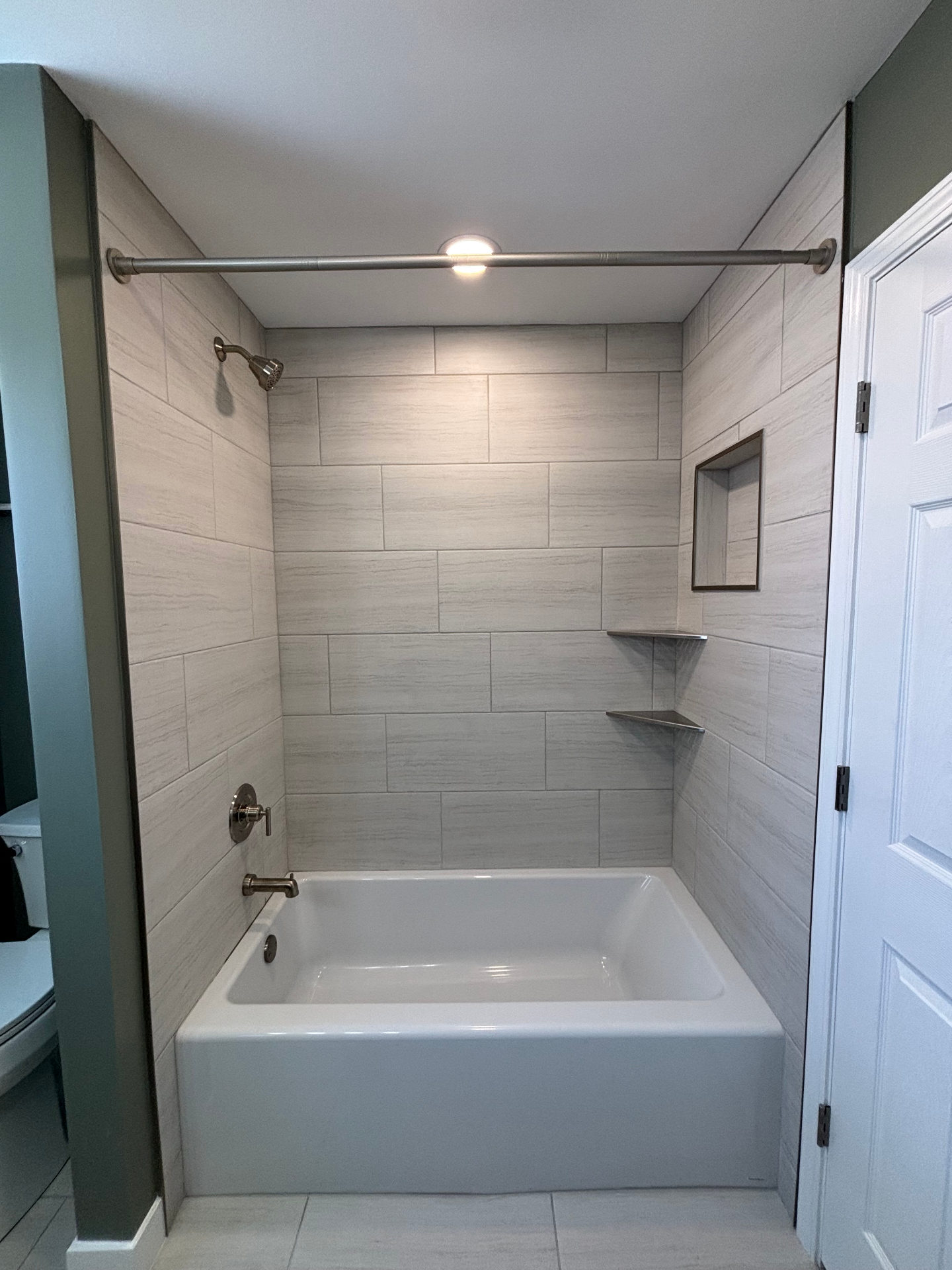 Light large-format tile tub and shower surround with brushed-nickel fixtures, recessed niche and corner shelves