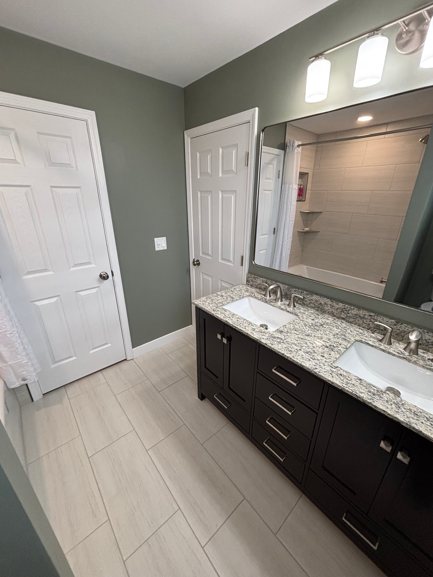 Sage-green bathroom with espresso double vanity, granite top, large framed mirror and tub/shower beyond