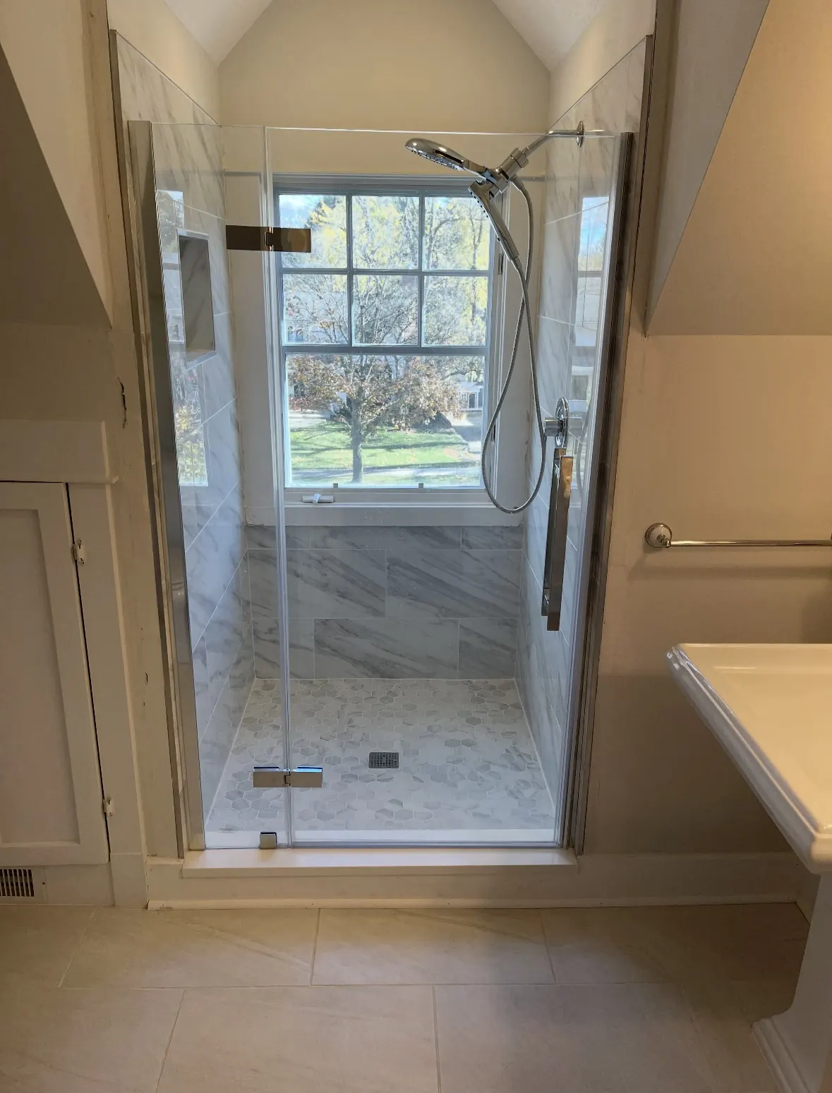 Completed Lincolnshire bathroom remodel by WK Bath Solutions featuring a frameless glass walk-in shower, marble tile walls, hexagon mosaic floor, and a sunlit window.
